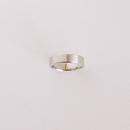 Above view of the Vow (Brushed) men’s wedding band standing on its side, showcasing the brushed 14k white gold finish against a soft background.