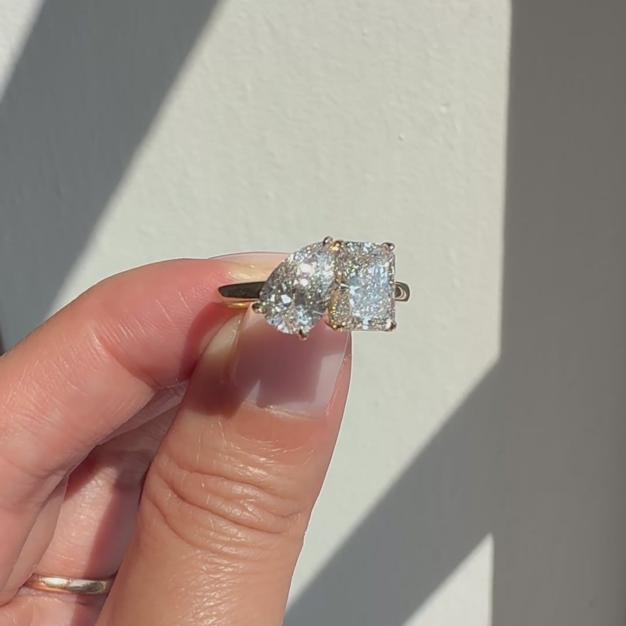 video of toi et moi gold ring with pear and radiant lab diamonds held in sunlight and sparkling as it moves